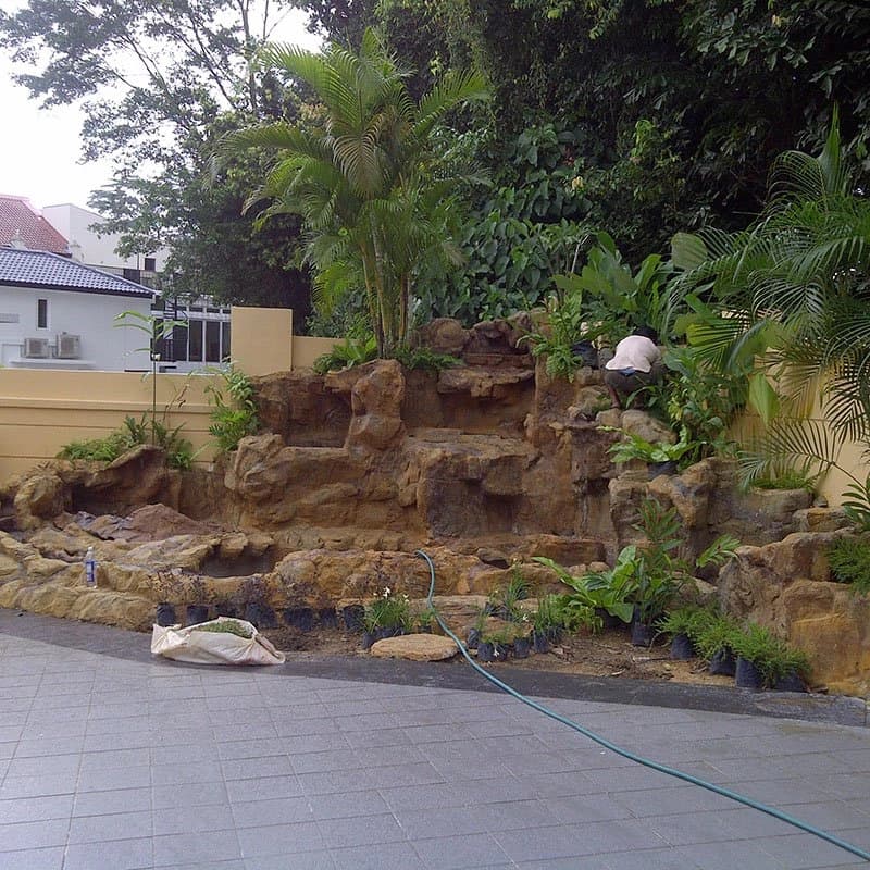 Rock waterfall and pond under construction with a crew member setting out plants
