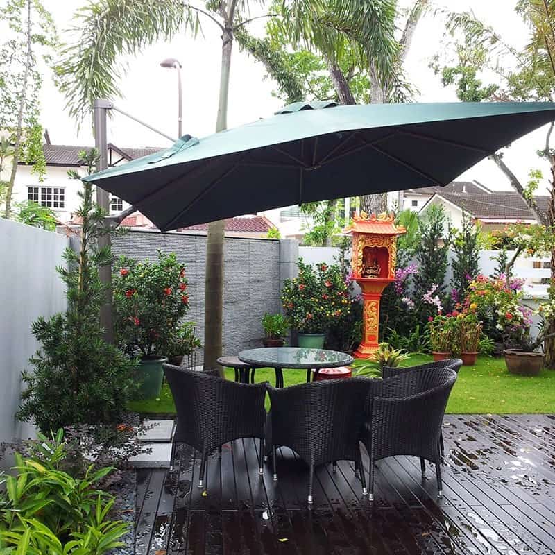 Timber deck with rattan dining set under a cantilever umbrella beside turf and flowering shrubs